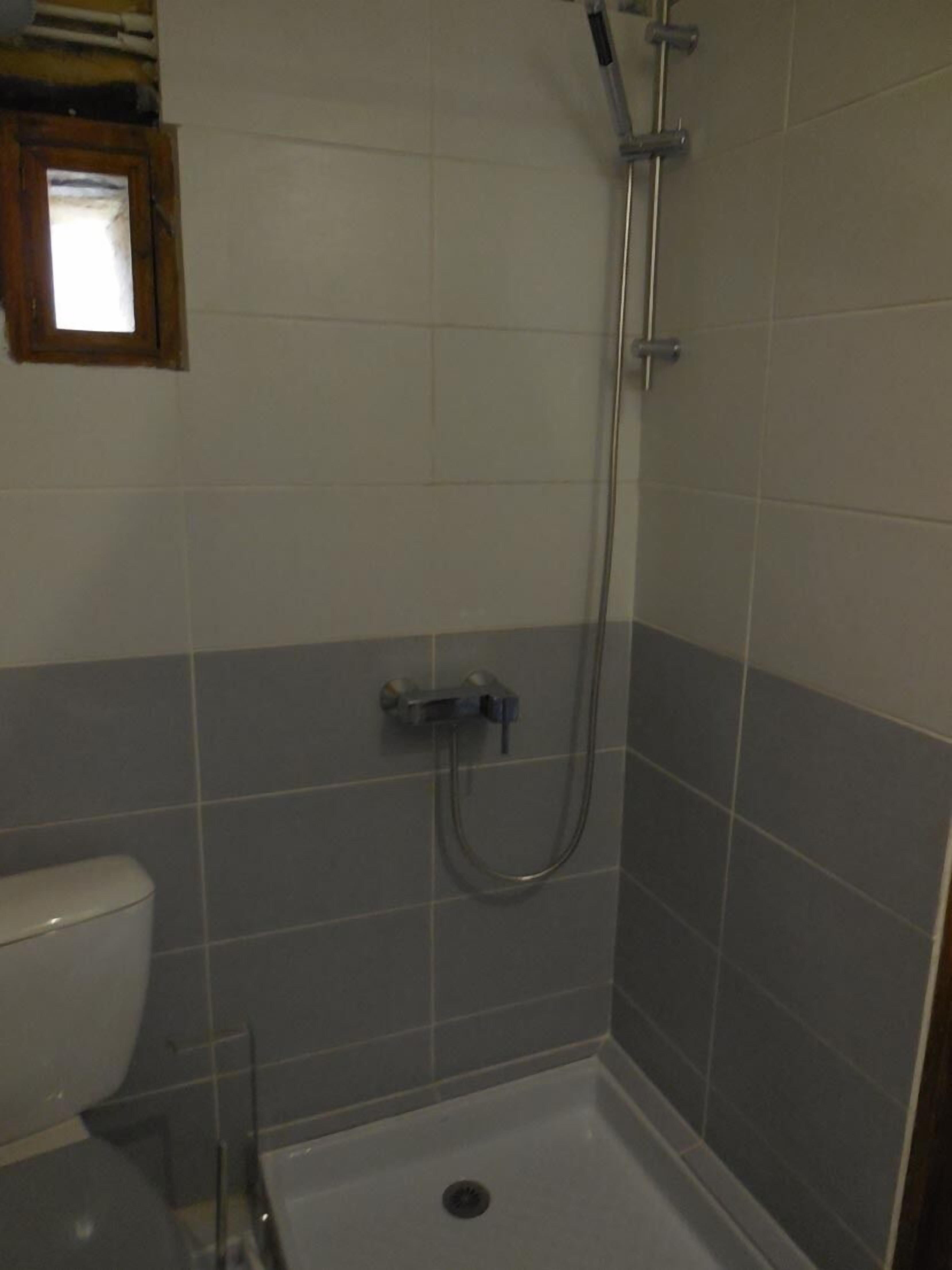 Une petite salle de bain avec une douche, des toilettes et une fenêtre.