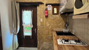A small kitchen with a stone wall, a wooden door, a gas stove, a sink, and a fire extinguisher. - Gîte 2p Lascaux, 2*, wifi, park, games, heated swimming pool, Spa, ok dogs & cats (MONTIGNAC-LASCAUX)