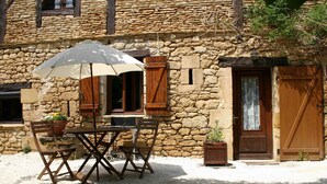 A stone building with a wooden table and chairs, an umbrella, and a door. - Gîte 2p Lascaux, 2*, wifi, park, games, heated swimming pool, Spa, ok dogs & cats (MONTIGNAC-LASCAUX)