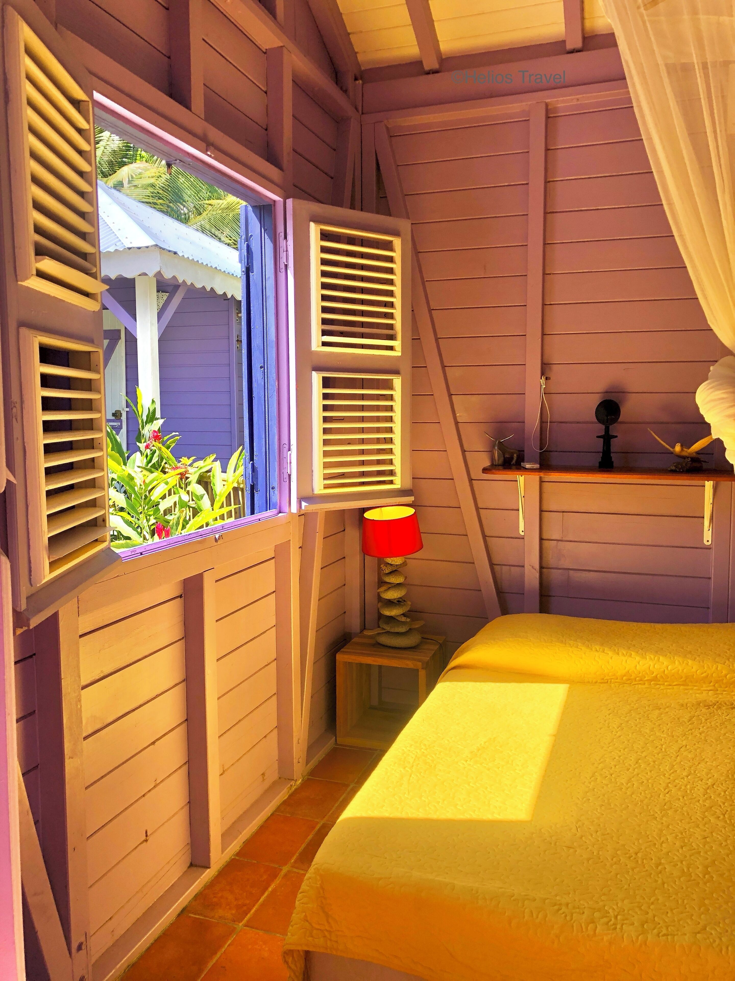 Un dormitorio con cama, ventana con contraventanas, una mesita de noche con lámpara y estante con un adorno.