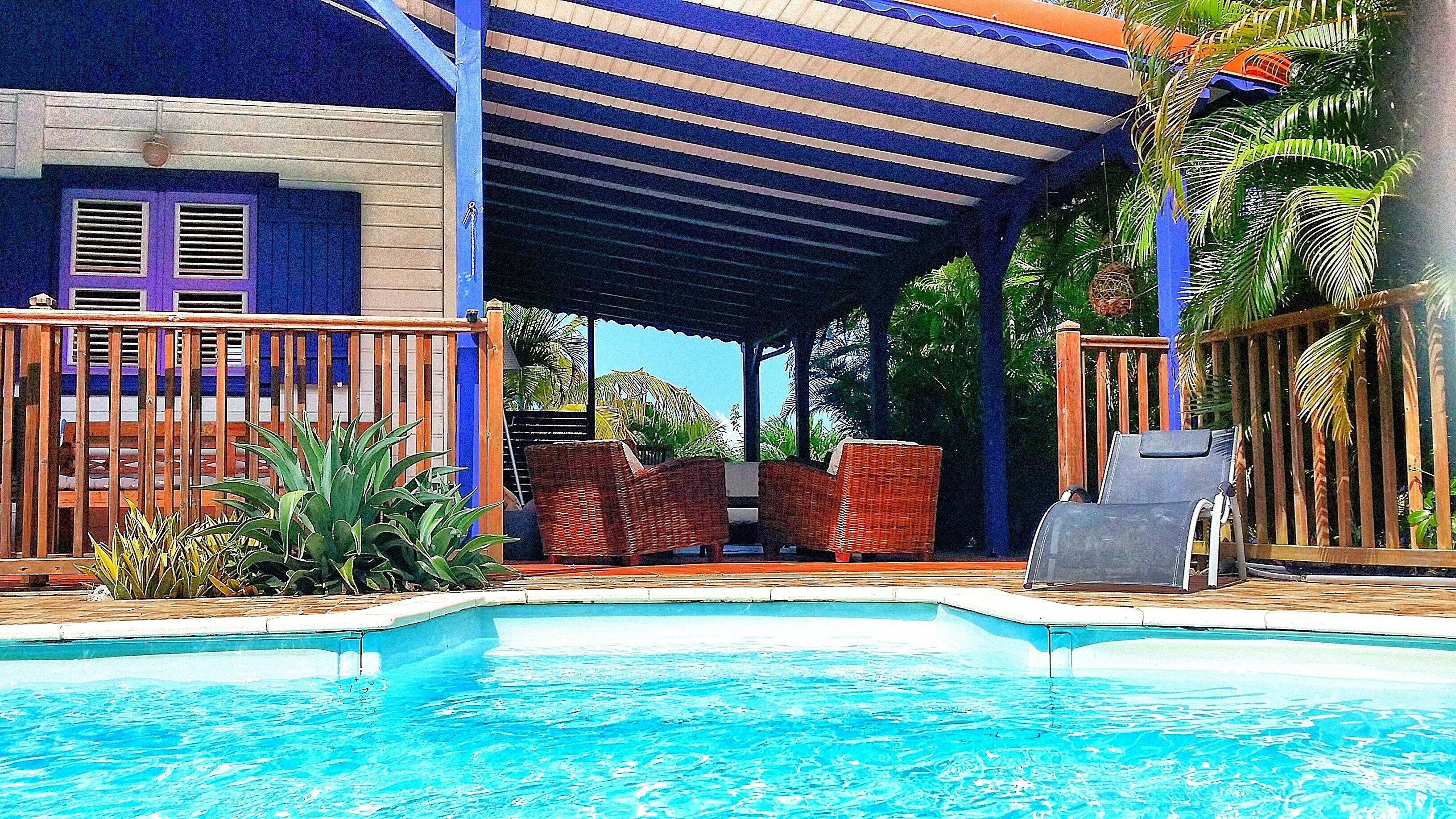 A pool area with a covered seating area, wicker furniture, and a view of the pool.