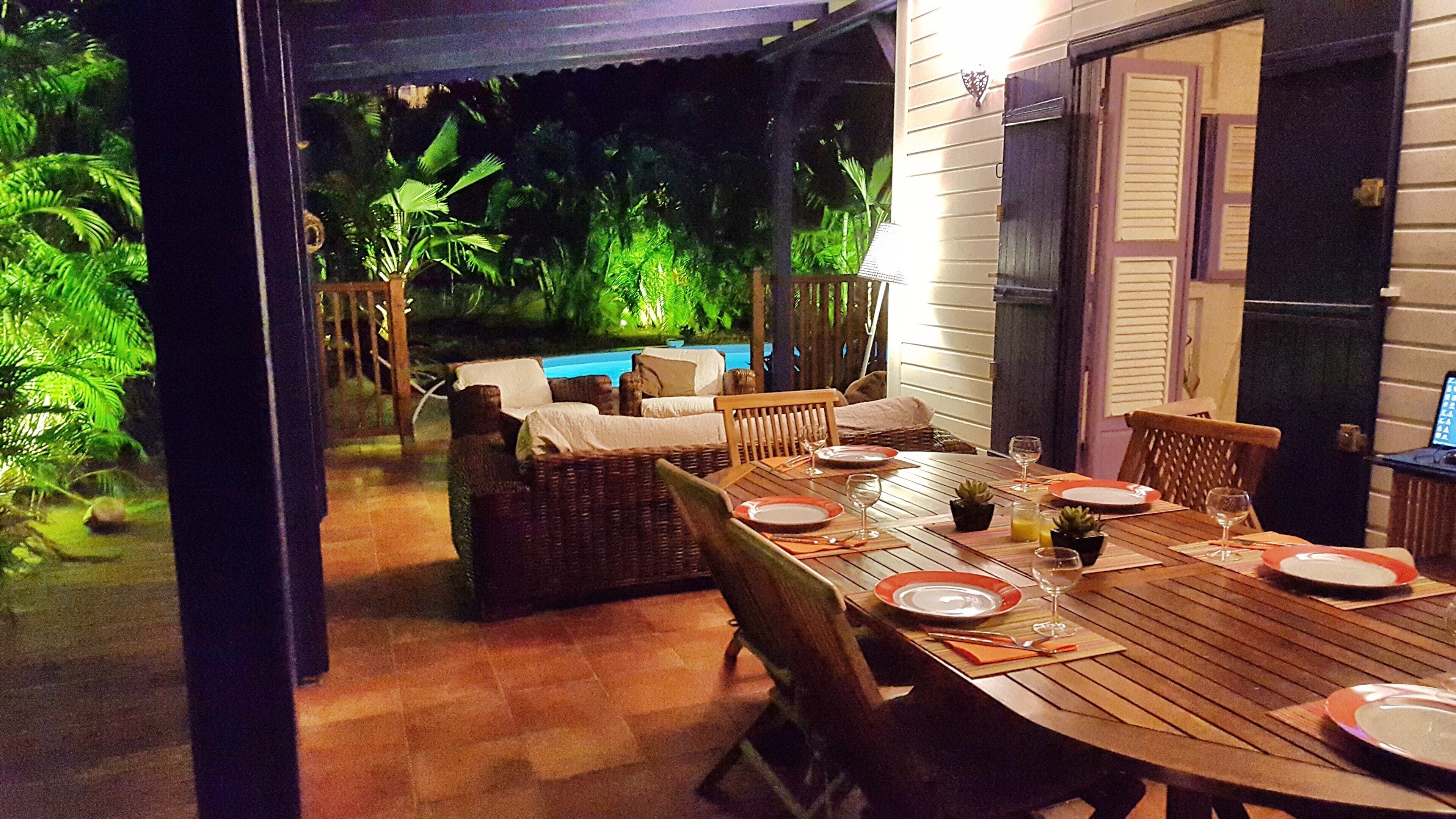 An outdoor dining area with a pool, wicker furniture, and a wooden table set for a meal.