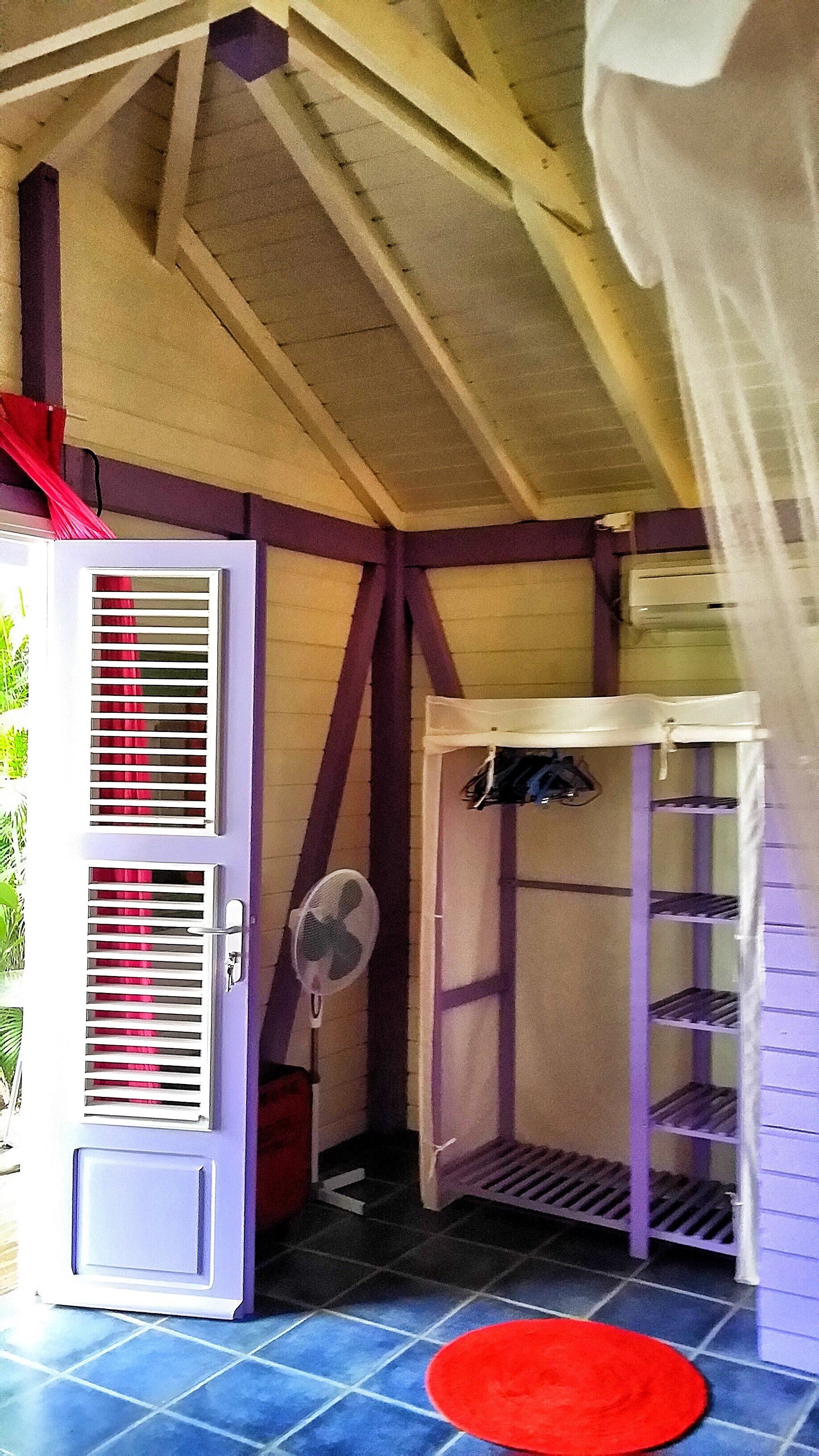 Ein Zimmer mit einer weißen Tür, einem roten Ventilator, einem roten Teppich und einem weißen Regal.