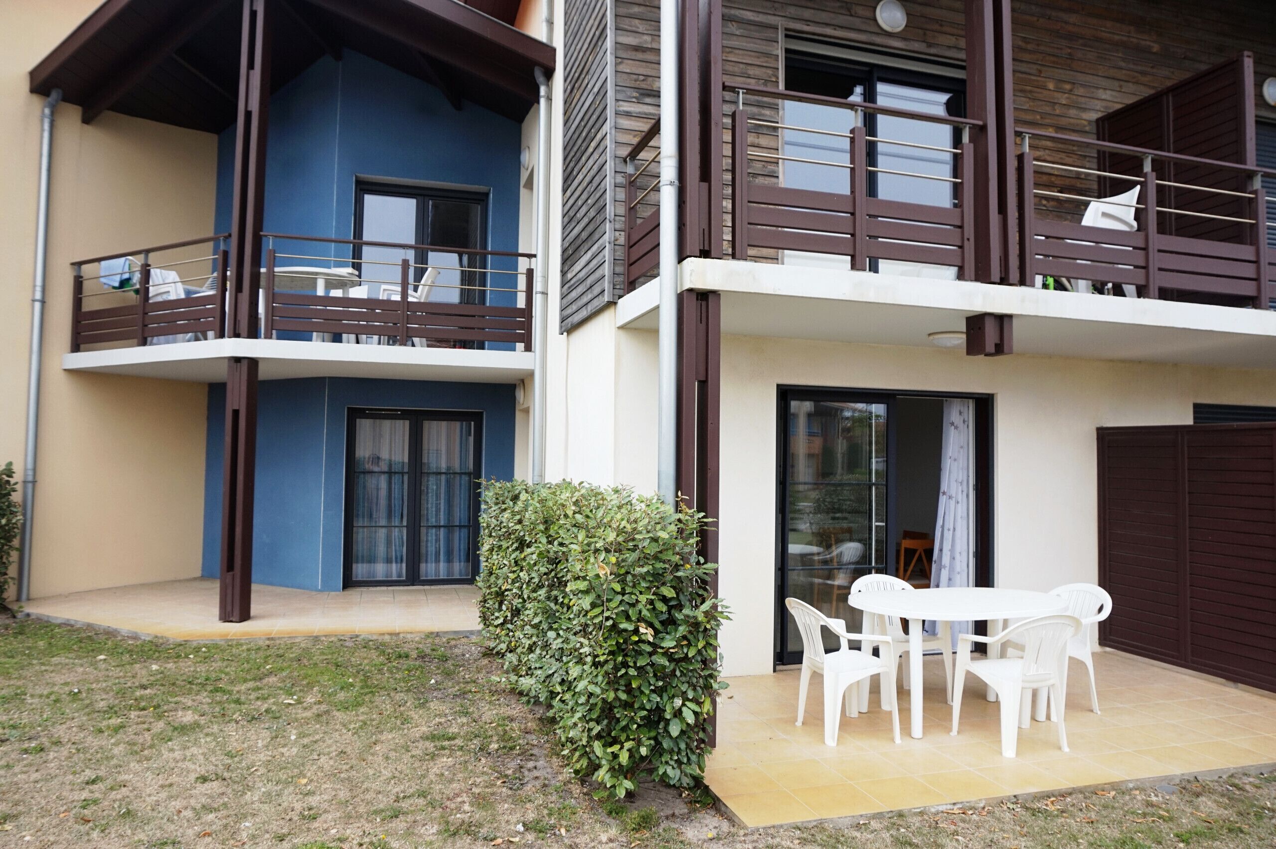 A two-story residential building with a balcony, a small garden, and a patio with outdoor furniture.