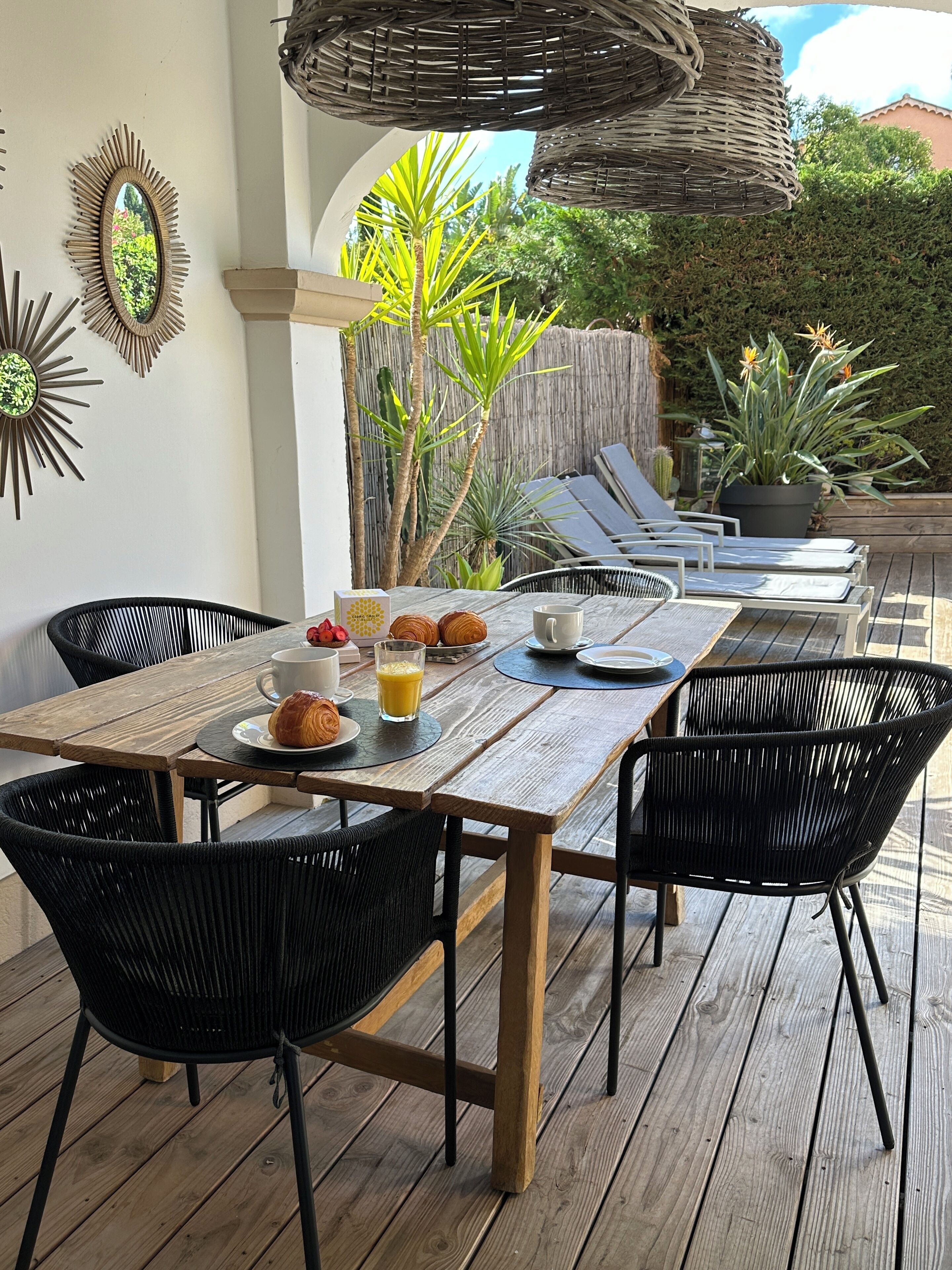 An outdoor dining area with a wooden table, black wicker chairs, and a wicker ceiling.