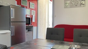 Une cuisine compacte équipée d’un réfrigérateur, d’un four à micro-ondes et d’une cuisinière, une table à manger avec des chaises et un canapé rouge.