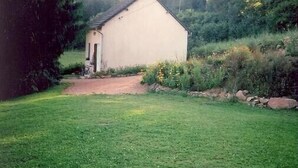 Un petit bâtiment d’un seul étage, doté d’un toit en pente, entouré d’une zone herbeuse et d’une végétation dense.