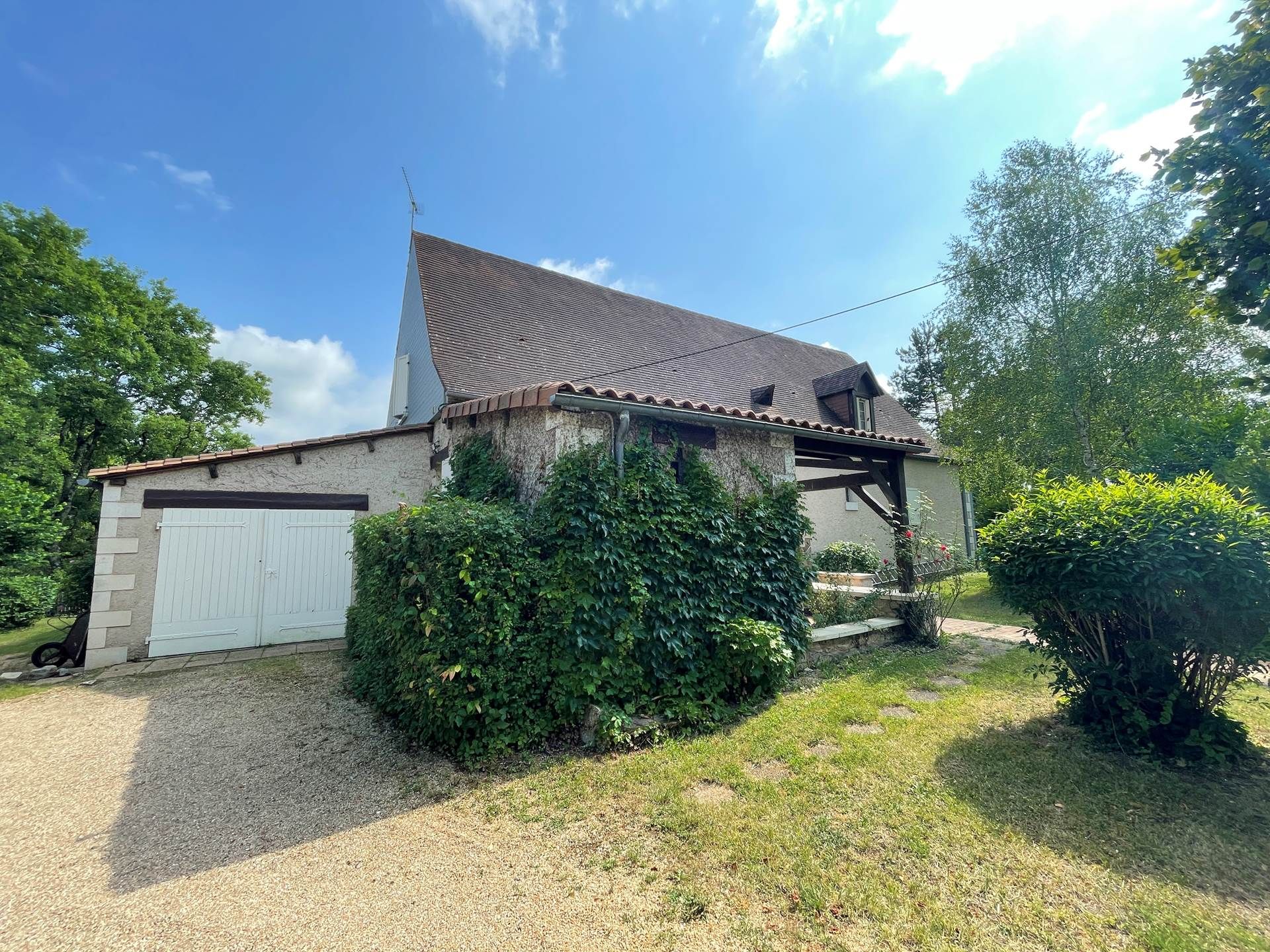 Une maison de plain-pied avec un toit en pente, une porte de garage blanche et une allée gravillonnée.