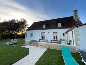 Une maison avec une pelouse bien entretenue, une terrasse dotée de mobilier d’extérieur et un ciel dégagé.