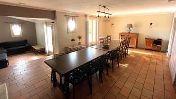 Un espace repas comprenant une longue table et des chaises, un canapé, une petite table avec une lampe et un buffet.