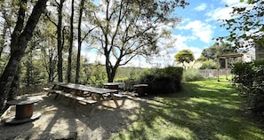 A picnic area with a wooden table and benches, surrounded by trees and a grassy lawn.