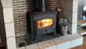Una chimenea de piedra con estufa de leña, un reloj encima y un balde metálico a la derecha.