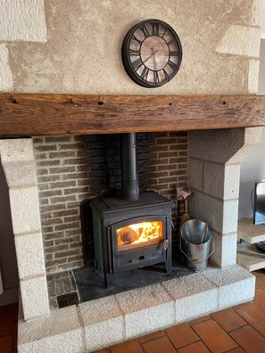Un poêle à bois, avec une horloge au-dessus, installé dans une cheminée en pierre.