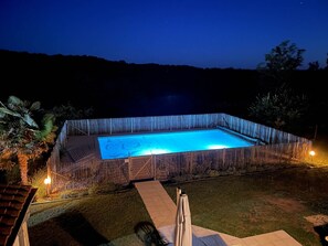 Ein rechteckiger Schwimmteich, umgeben von einem Holzzaun, mit freiem Blick auf den Himmel und sanfte Hügel in der Ferne.