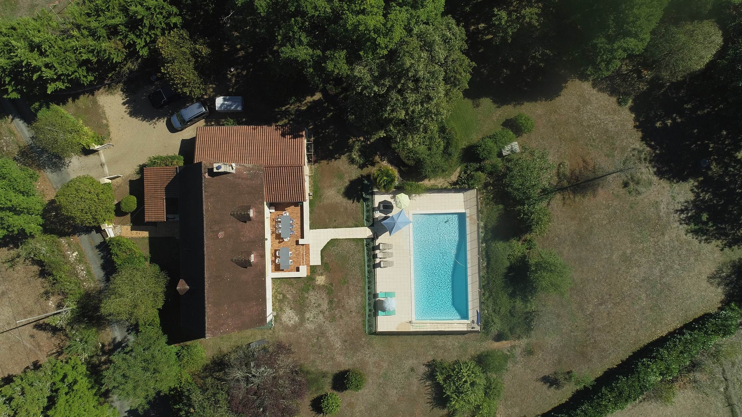 An aerial view of a property with a swimming pool, a covered patio, and a car parked nearby.