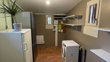 Une cuisine compacte équipée d’un réfrigérateur, d’un lave-linge et agrémentée d’une plante en pot.