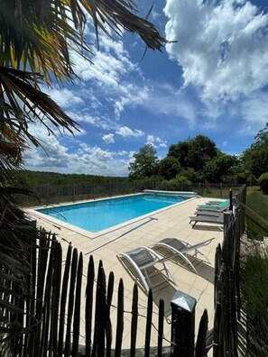 Une piscine rectangulaire avec une terrasse carrelée et des chaises longues.
