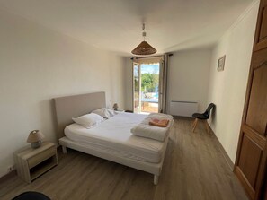 Ein Schlafzimmer mit einem Bett, einem Nachttisch, einem Sessel, einem Deckenventilator und Blick auf ein Außenbecken.