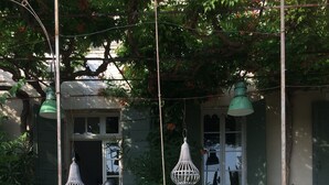 A quaint garden with a stone bench, hanging white lanterns, and a small table with chairs.