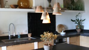 A kitchen with a central island, pendant lights, a black backsplash, and various kitchen items.