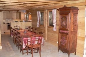 Interior em madeira com uma longa mesa de jantar posta para seis pessoas, armários de madeira e um grande aparador de madeira com esculturas detalhadas.