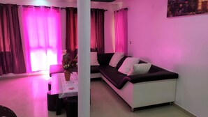 Una sala de estar con un sofá, una mesa de comedor con un florero y cortinas rosas.