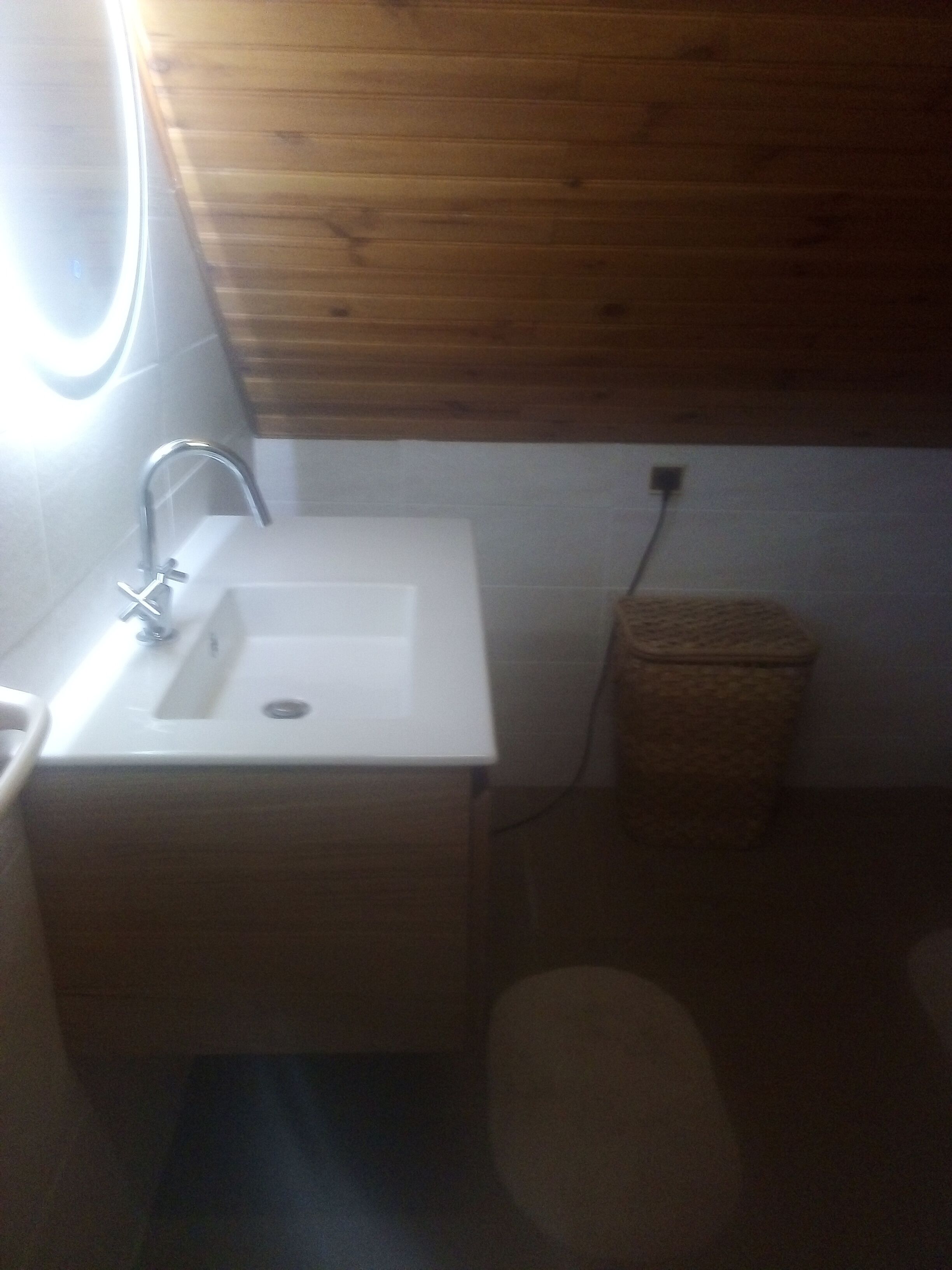 Une petite salle de bain avec un plafond en bois, un lavabo blanc et une poubelle.
