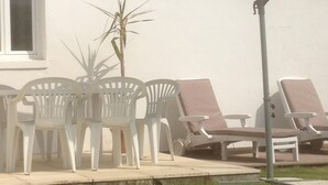Un espace patio avec des chaises en plastique blanches et un parasol violet, un petit palmier et un toit recouvert de tuiles.