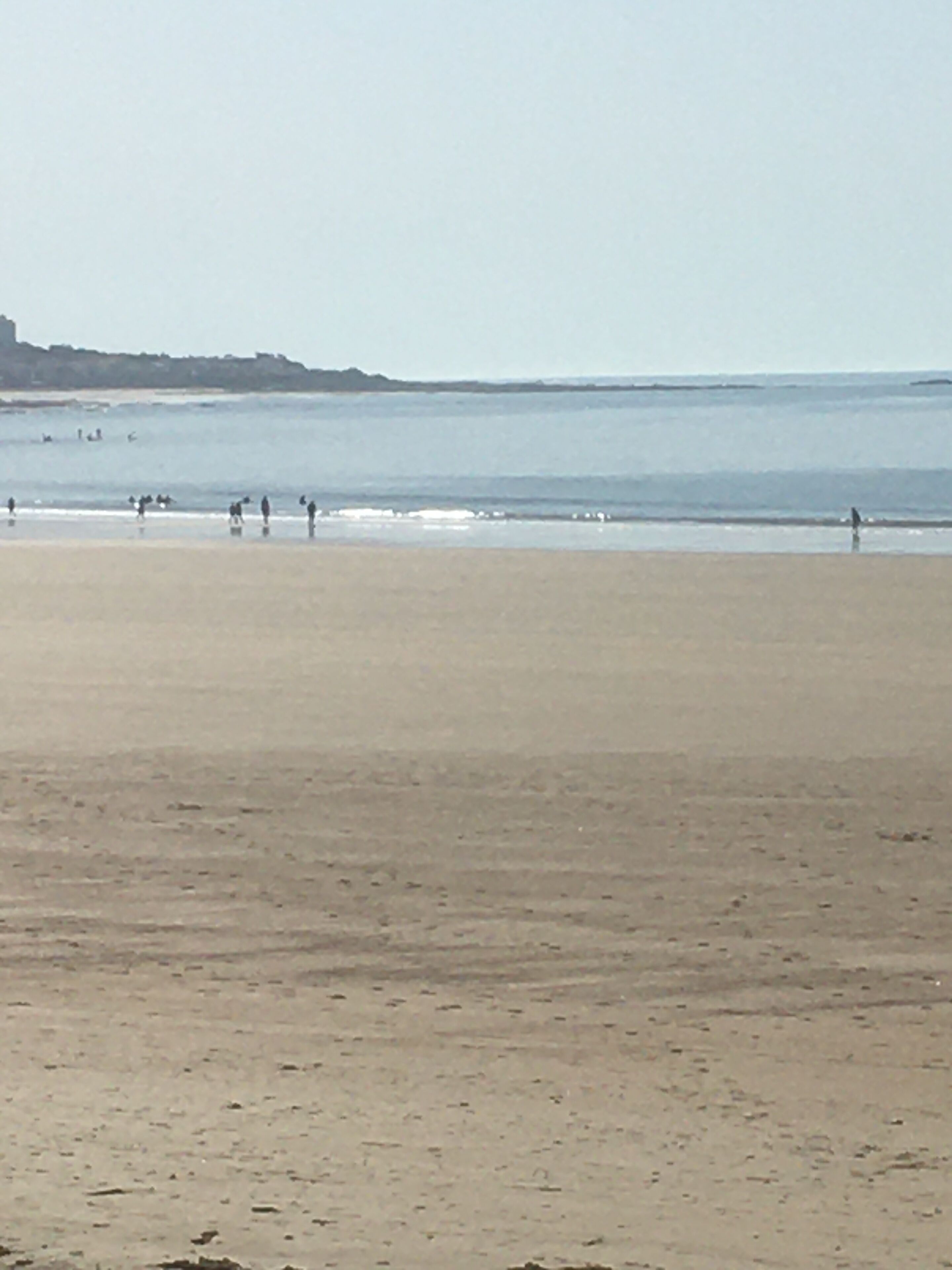 A wide sandy beach with a calm sea and a distant shoreline.