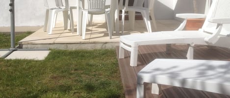 An outdoor patio with white plastic chairs and a table, a purple umbrella, and a wooden deck.