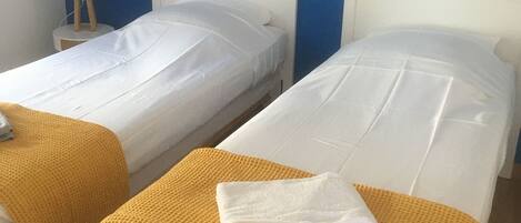 Two single beds with white linens and a yellow throw blanket on one bed.