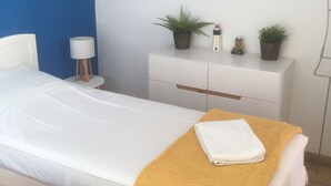 Une chambre à coucher avec un lit, une table de chevet, une lampe, une commode et un tableau représentant une scène de plage.