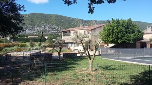 Un paysage rural avec un mur de pierres, une zone délimitée par une clôture et un bâtiment doté d’un toit en tuiles.