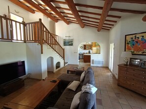 Relax in this spacious living area with a high ceiling, featuring a large flat-screen TV, comfortable sofa, and wooden coffee table.