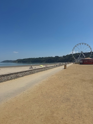 A beach with a sandy shore, a stone wall, and a large Ferris wheel in the background.