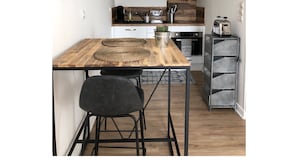 A compact kitchen with a wooden table, two black chairs, a coffee machine, and a built-in oven. - Charming Studio Facing the Port and 100 m from the beach (Binic)