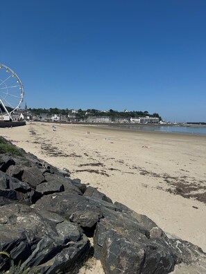 A beach with a large Ferris wheel, rocky shoreline, and buildings in the background.