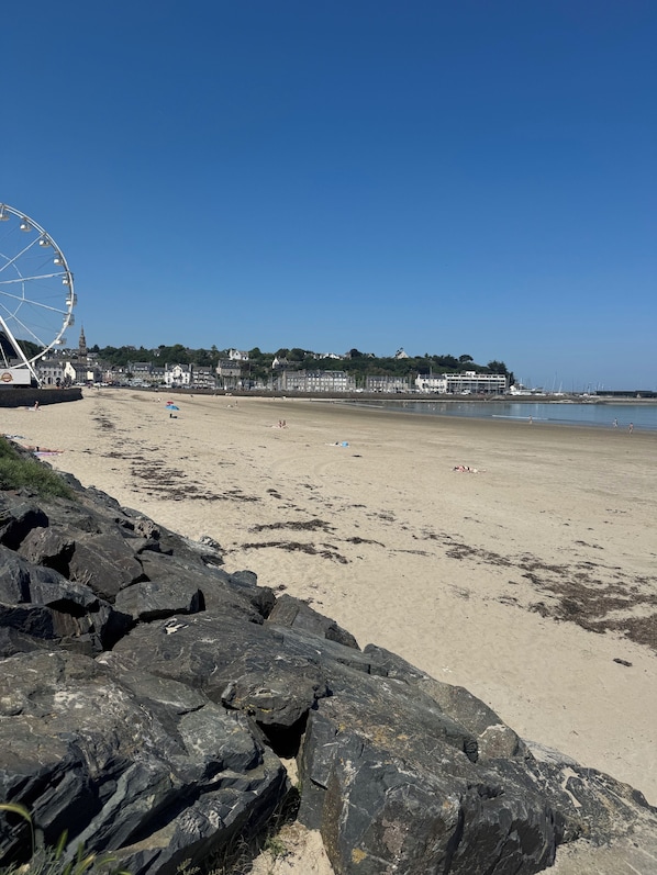 A beach with a large Ferris wheel, rocky shoreline, and buildings in the background.