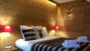 Une chambre confortable avec un mur en bois, un lit avec une literie blanche, deux lampes rouges et un coussin à motifs de cerf.
