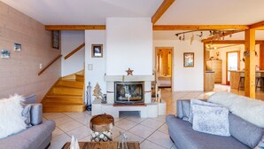Un salon moderne avec une cheminée, un escalier en bois et des fauteuils confortables.
