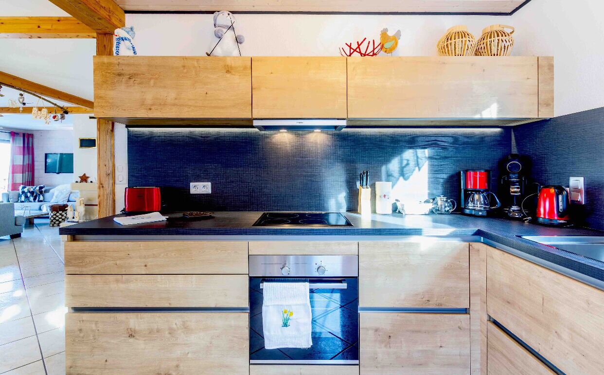 Une cuisine moderne avec des meubles en bois, un four encastré et un crédence noire.