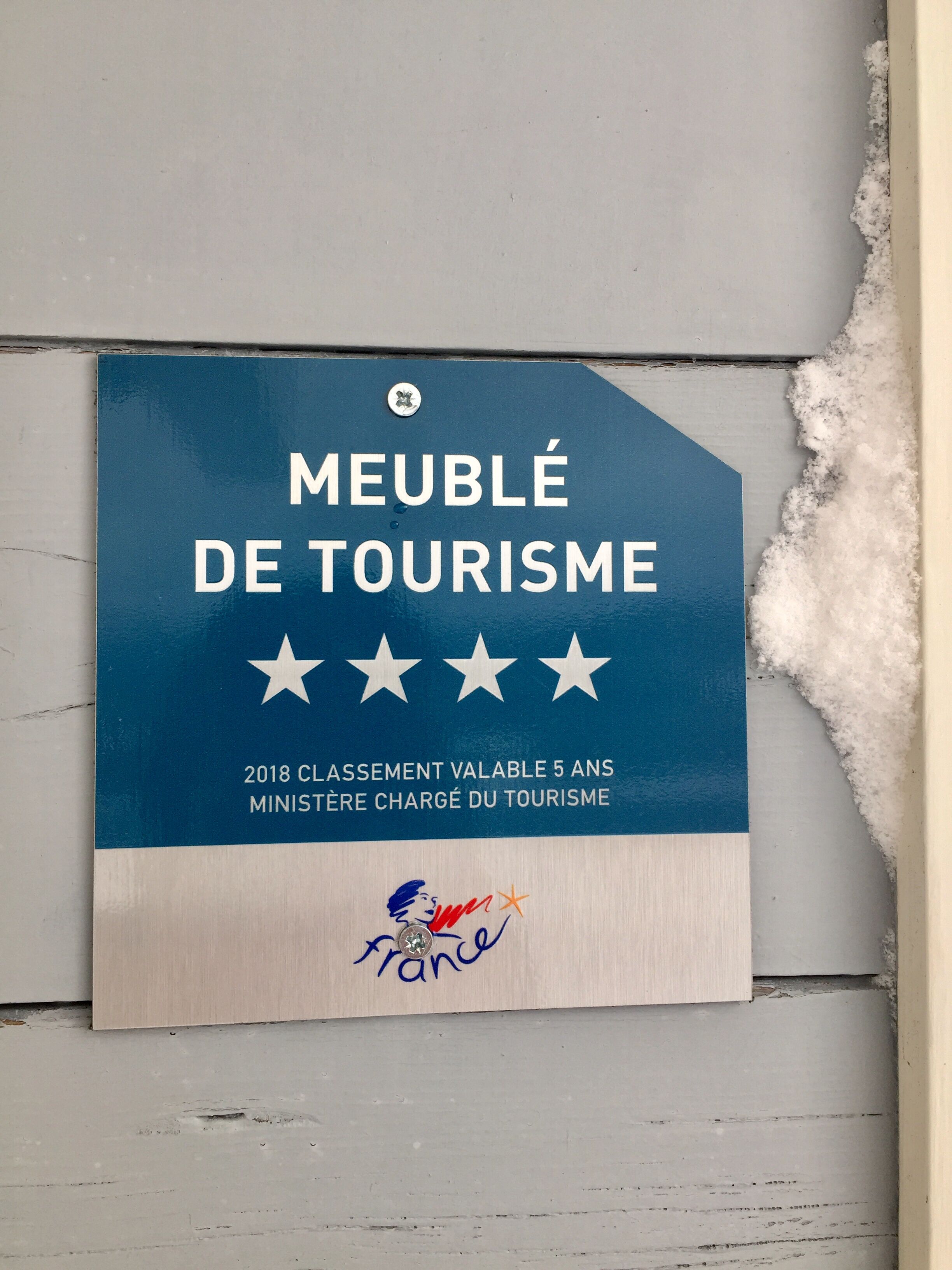 A blue sign with white text stating "MEUBLÉ DE TOURISME" and "2018 CLASSEMENT VALABLE 5 ANS MINISTÈRE CHARGÉ DU TOURISME".