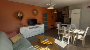 A living room with a sofa, coffee table, TV, and dining area with chairs and a table. - South-facing, cocooning gîte 40 m from the sea, rated 3***. (Fécamp)