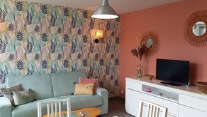 A living room with a sofa, a TV, a white cabinet, and patterned wallpaper. - South-facing, cocooning gîte 40 m from the sea, rated 3***. (Fécamp)