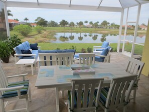 Un porche cubierto con mesa y sillas, vista a un lago y vegetación circundante.