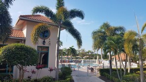 Un complejo turístico con piscina, palmeras y un edificio de techo a la española y un reloj.