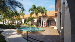 A pool area with a tiled edge, surrounded by palm trees and a building with a tiled roof. - Beautiful 3 Bedroom 2 Bath Home in a Resort-like Community.   (North Fort Myers)