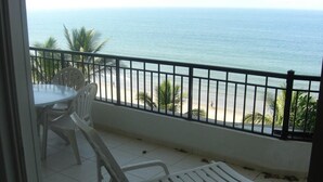 A balcony with a view of the ocean, a table, and two white chairs.