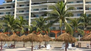 A multi-story hotel with balconies, palm trees, and thatched umbrellas.