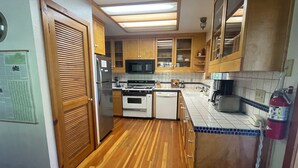 Une cuisine équipée de meubles en bois, d’un réfrigérateur, d’une cuisinière, d’un four à micro-ondes et d’un extincteur.